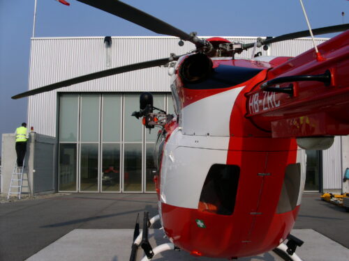 helicopter landed on a heliport. A worker is installing a obstruction light on a hangar